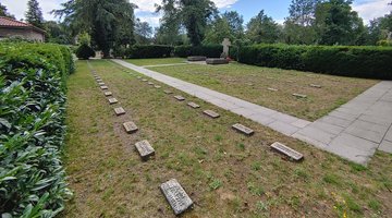Zu sehen ist die Kriegsgräberstätte Osnabrück-Eversburg. Man sieht die einzelnen Grabsteine gereiht. Im Hintergrund sieht man Bäume und Gebüsch.