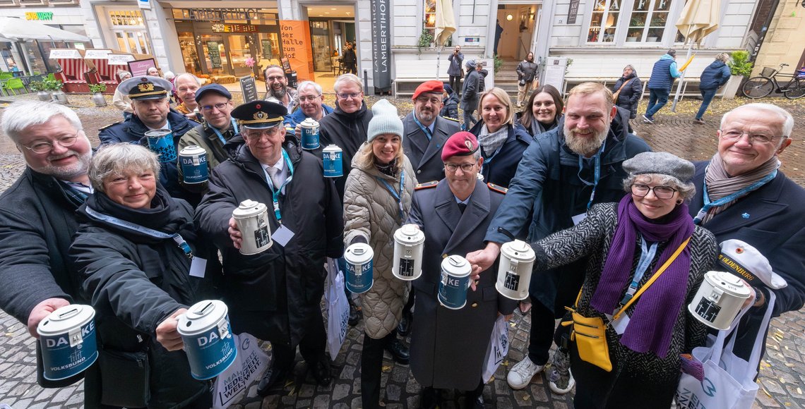 Menschengruppe blickt in Richtung Kamera und hält Sammeldose des Volksbunds ausgestreckt vor sich 