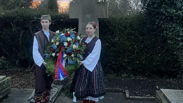 Zu sehen sind die beiden Jugendlicher in Traditionskleidung. Sie halten den Kranz in der Hand. Der Kranz ist in den Farben der serbischen Nationalflagge gestaltet. Die Jugendlichen schauen in Richtung Kamera.