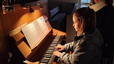 Zu sehen ist das Mädchen sitzend an der Orgel, die die Musikstücke spielt.