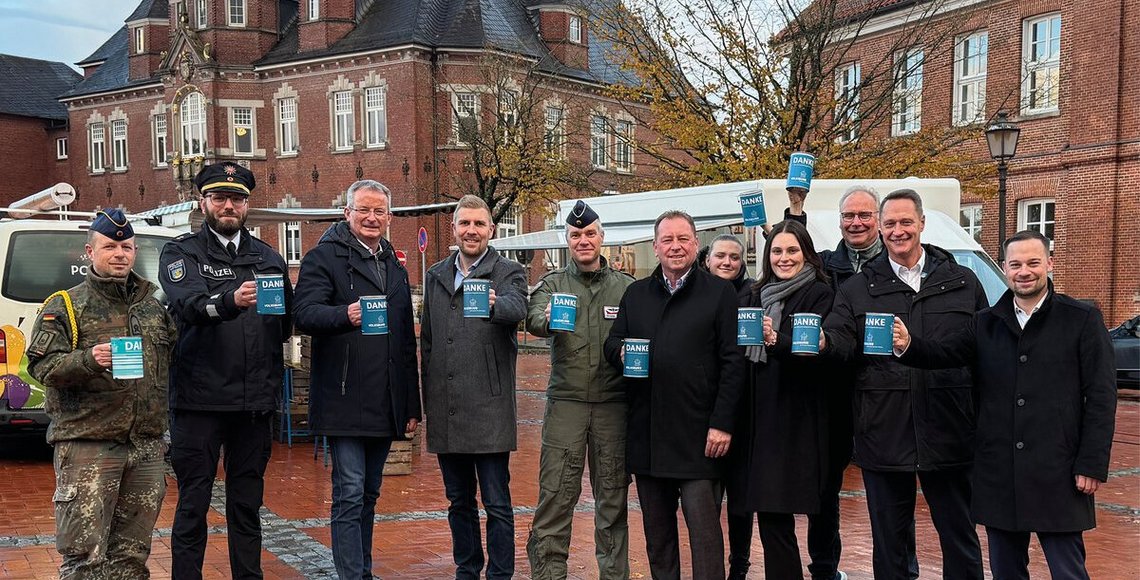 Elf Personen posieren vor dem alten Kreishaus in Wittmund, auf dem Marktplatz stehend, mit Sammeldosen in der Hand für ein Foto