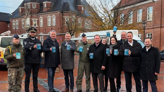 Elf Personen posieren vor dem alten Kreishaus in Wittmund, auf dem Marktplatz stehend, mit Sammeldosen in der Hand für ein Foto